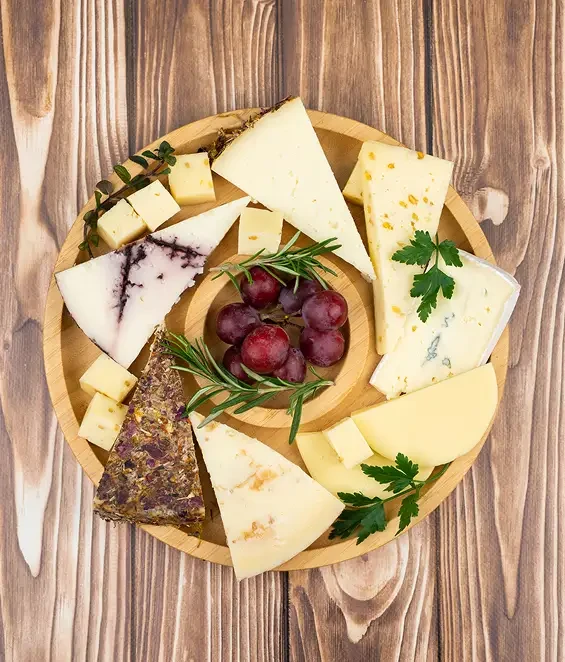 A round cheese board arranged around a bowl of grapes