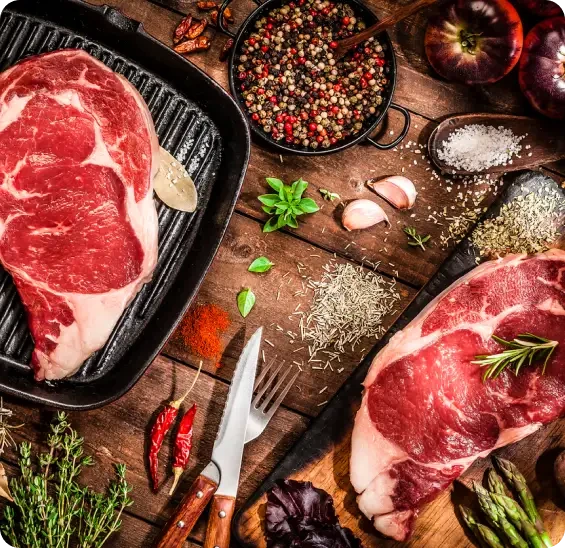 Raw steaks arranged beside herbs, peppercorns and garlic