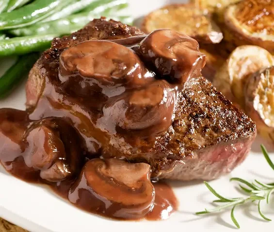 A steak topped with mushroom sauce beside roast potatoes