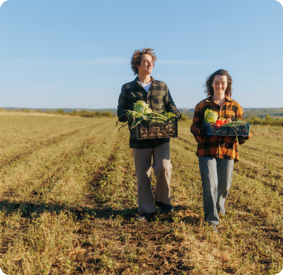 Two growers walking through a field carrying produce