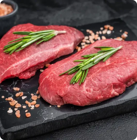 Two raw steaks topped with rosemary on a dark board