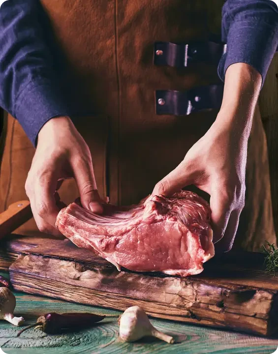 A butcher holding a raw rack of ribs on a chopping board