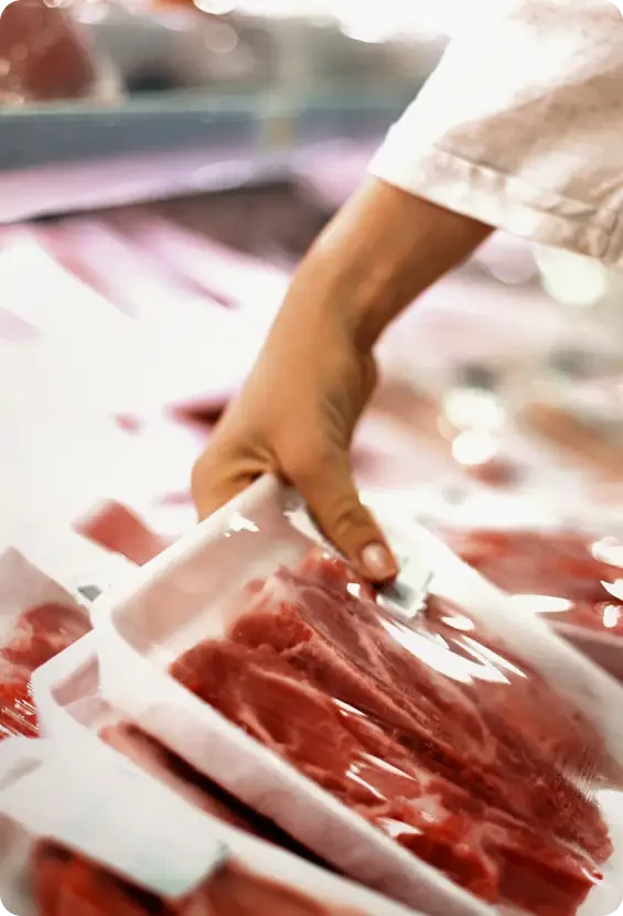A hand holding a tray of raw meat at a butcher's counter