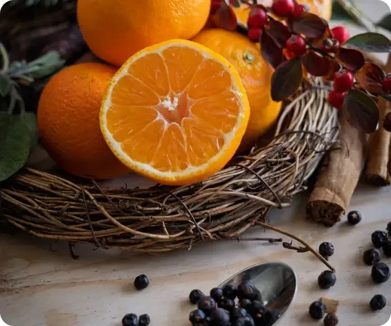 Whole and halved oranges in a wicker basket beside spices and berries