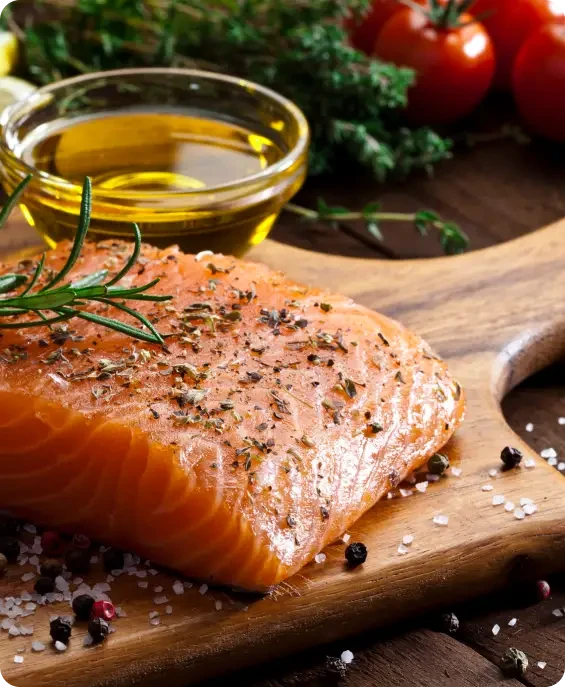 A seasoned raw salmon fillet beside oil and herbs
