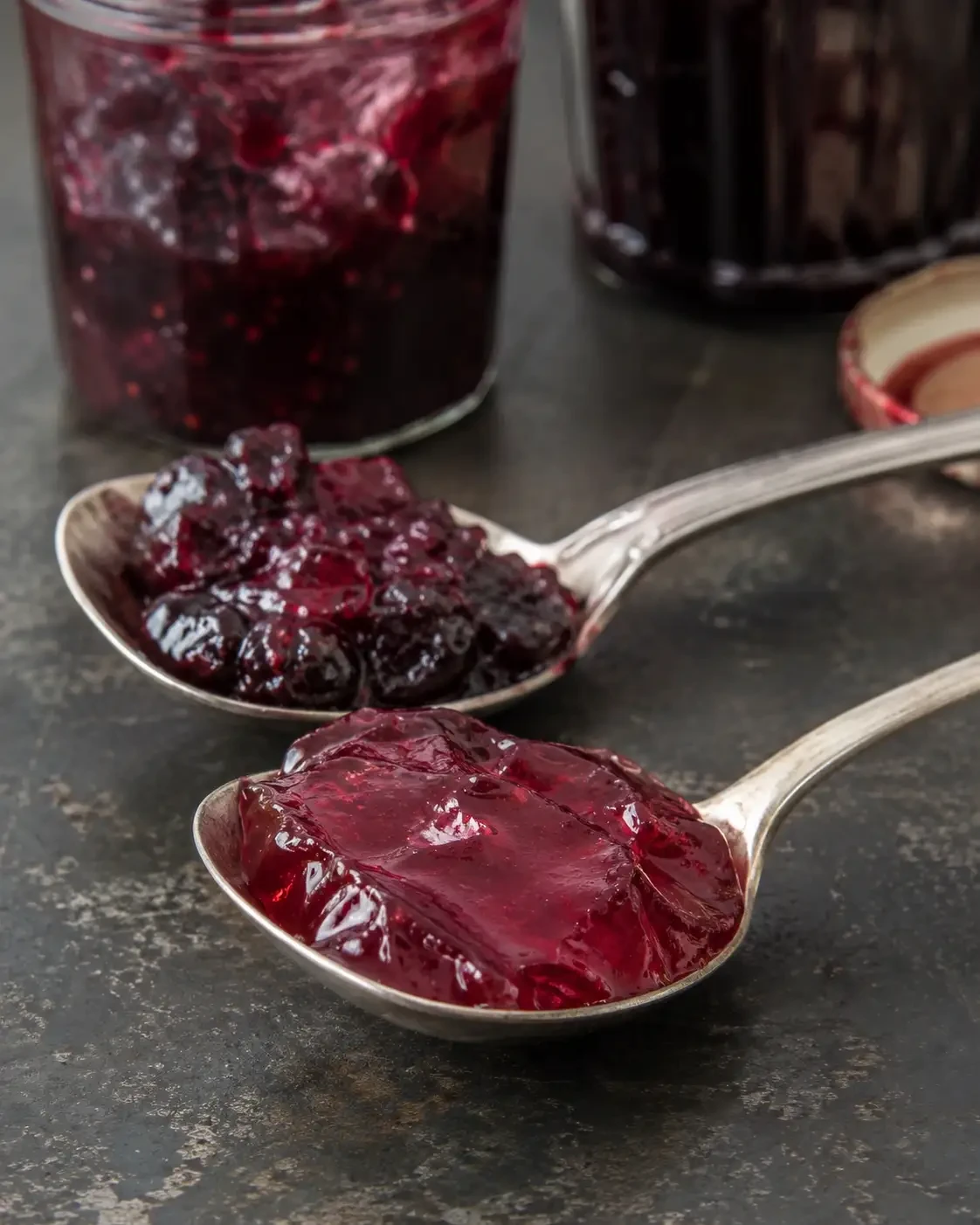 Spoons holding chunky berry preserve and smooth red jelly