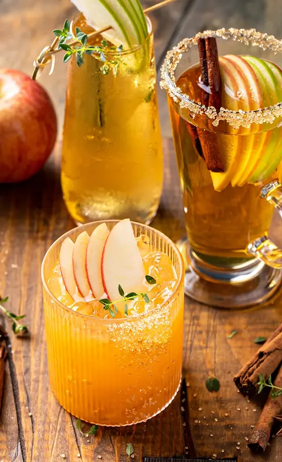 Golden drinks garnished with apple slices and herbs