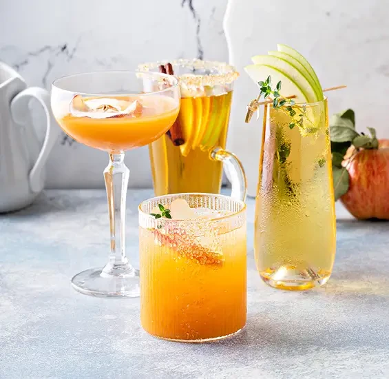 An assortment of fruit drinks with apple slices and herb garnishes