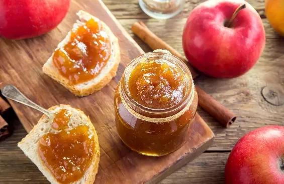 Apple jam on bread beside a jar, apples and cinnamon