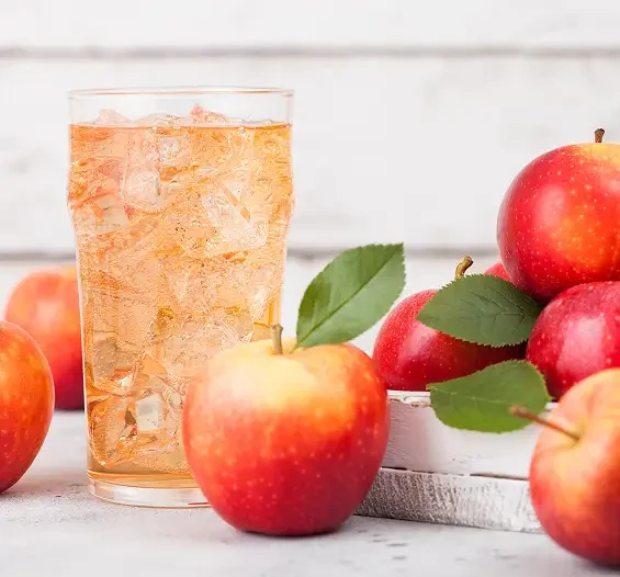 A glass of apple drink with ice beside red apples