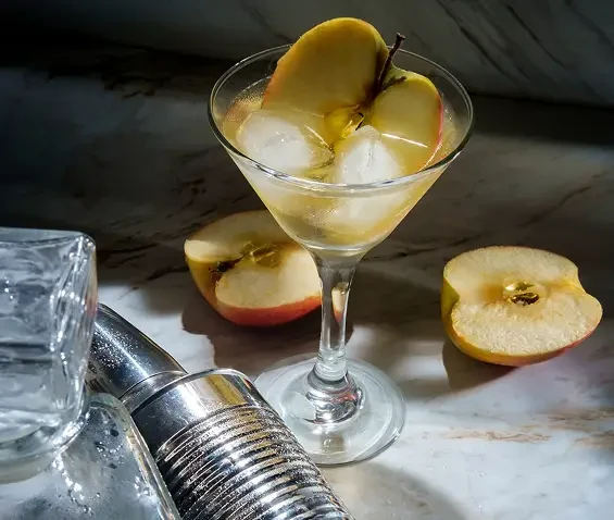 A pale drink with ice and apple slices in a stemmed glass