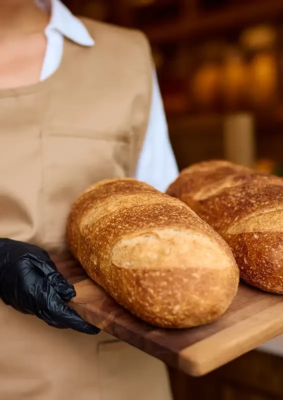 A baker holding a board of round bread loaves