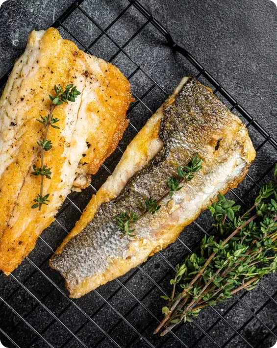 Two cooked fish fillets on a wire rack with herbs