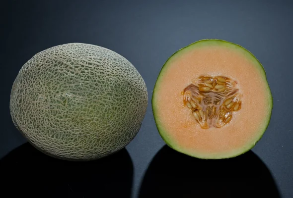A whole netted cantaloupe and a cut half with orange flesh on a dark background