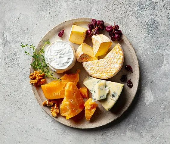 An assortment of cheeses arranged on a plate with grapes and walnuts