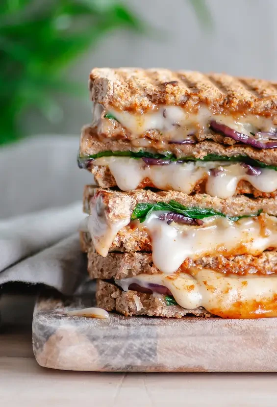 Stacked toasted sandwiches filled with melted cheese and greens