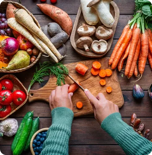 Hands slicing carrots beside a selection of fresh vegetables