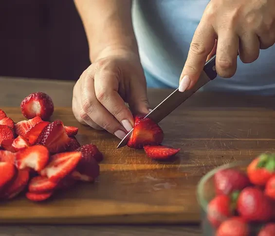 Hands slicing strawberries on a wooden chopping board