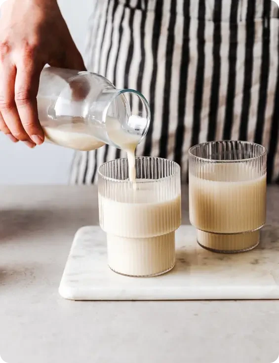 A person pouring milk into one of two glasses