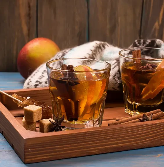 Two amber drinks served with apple slices and spices