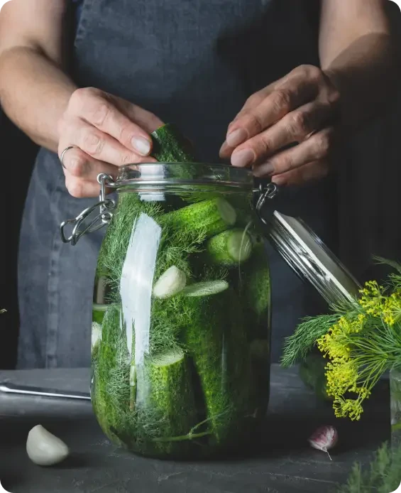 Hands packing cucumbers into a large glass jar