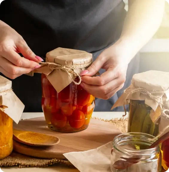 Hands tying a paper cover around a jar of preserved vegetables