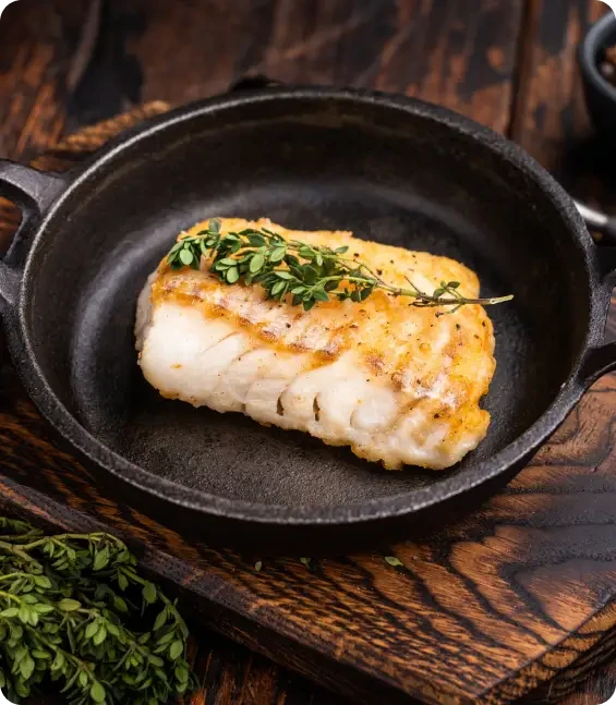 Cooked fish fillet topped with herbs in a frying pan