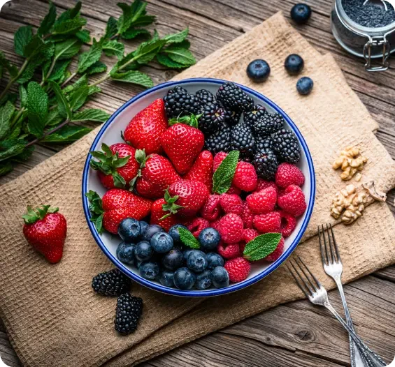 Fresh berries including strawberries, raspberries, blueberries and blackberries in a blue-rimmed bowl on rustic wooden table