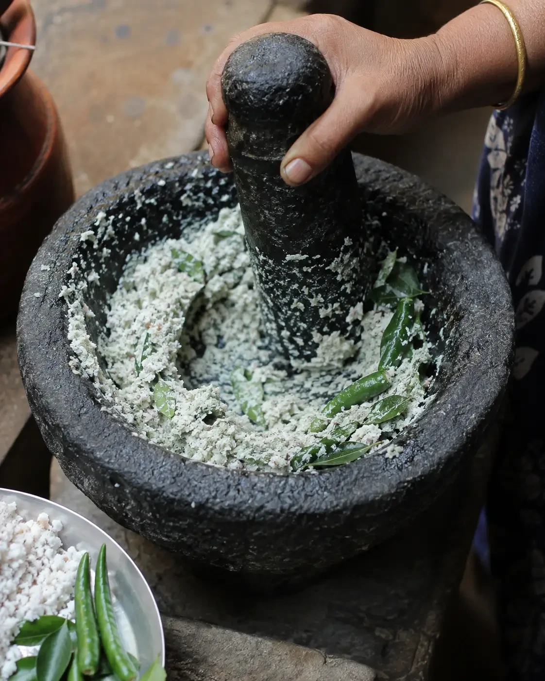 A hand grinding pale ingredients and green herbs with a stone pestle