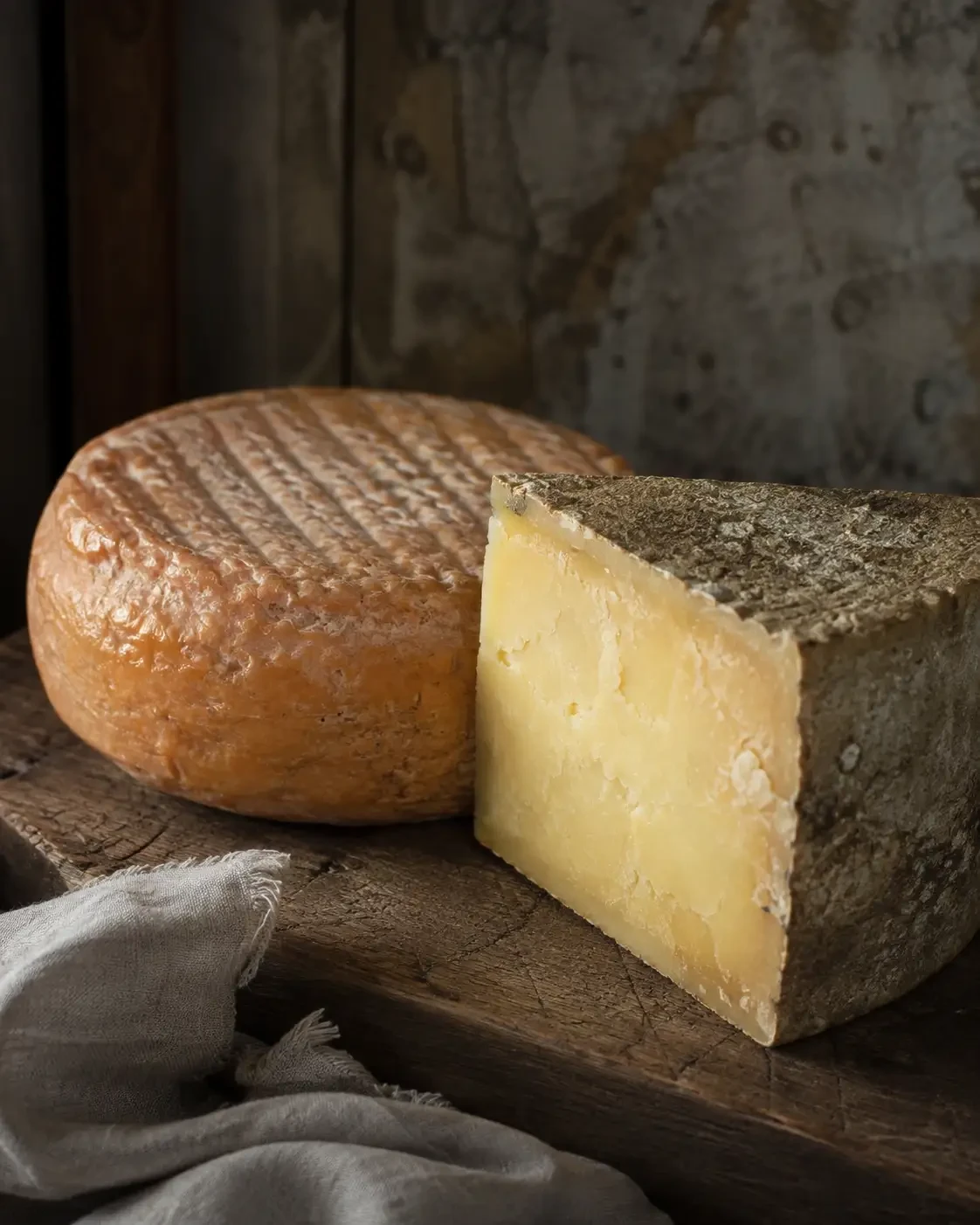 A hard cheese wedge beside a round cheese wheel