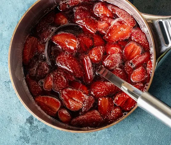 Halved strawberries cooking in a saucepan with a spoon