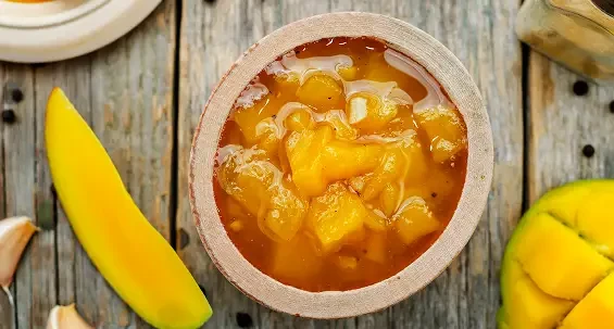 A bowl of golden fruit chutney beside sliced mango