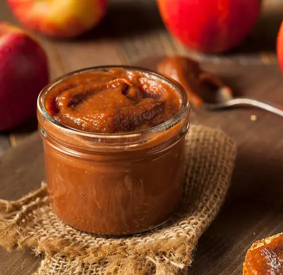 A jar of thick brown fruit spread beside apples