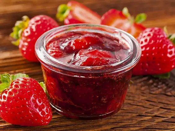 A small open jar of strawberry jam beside fresh strawberries