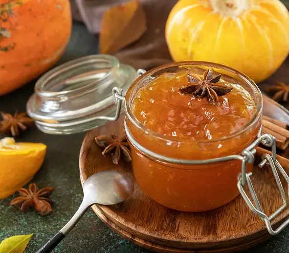 A jar of orange preserve beside citrus fruit and star anise
