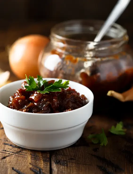 Dark chutney in a white bowl beside an open jar