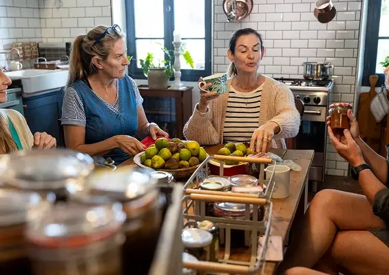 People talking around a kitchen table with fruit and jars of preserves