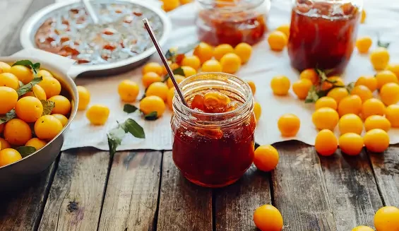 A jar of red fruit preserve surrounded by small yellow fruits