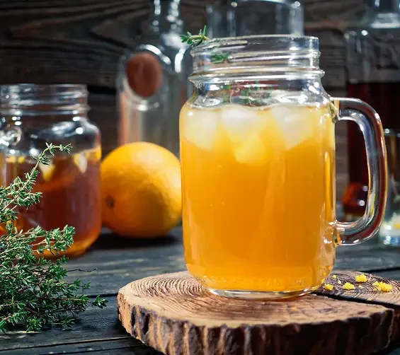 A golden iced drink in a handled glass beside citrus fruit and herbs