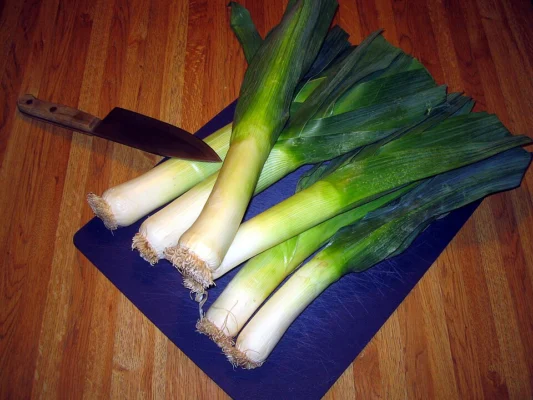 Fresh leeks on a cutting board beside a kitchen knife