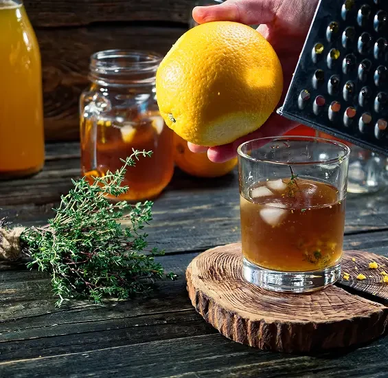 A lemon and grater held over a drink beside honey and herbs