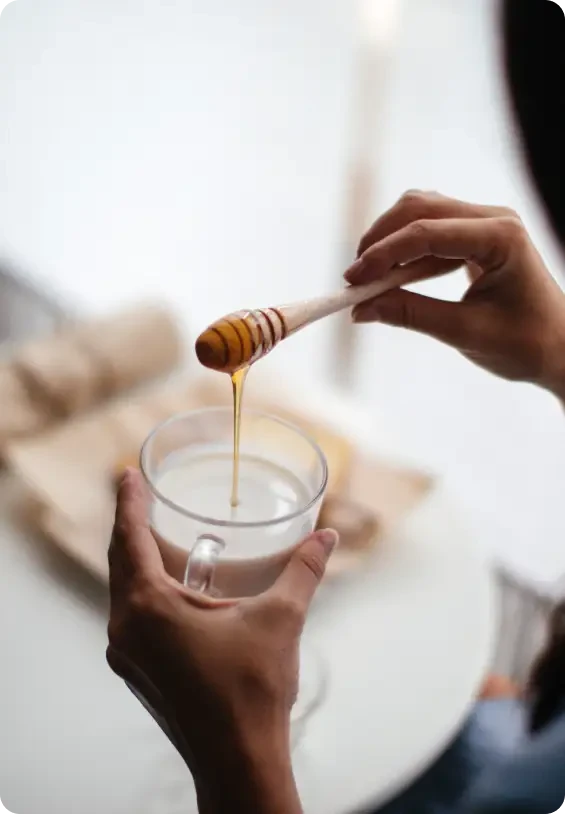Honey being drizzled into a glass of milk