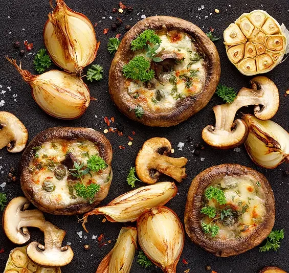 Stuffed mushrooms beside roasted garlic and onions