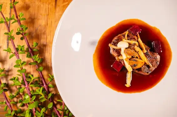 A plated dish topped with slender mushrooms and surrounded by red sauce