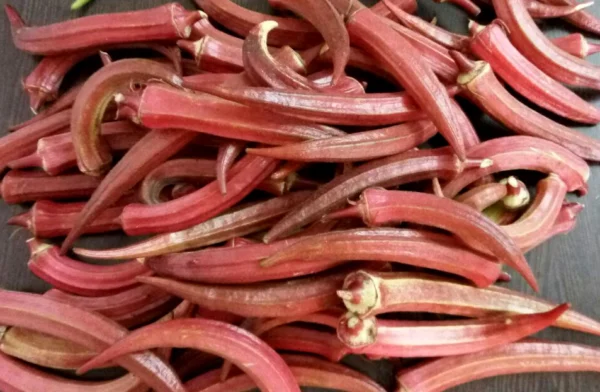 A pile of long red okra pods with pale cut stalk ends