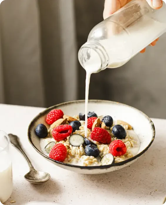 Milk being poured over a bowl of cereal and berries