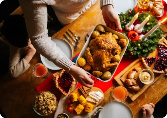 Person placing roast poultry and potatoes on a table set for a meal