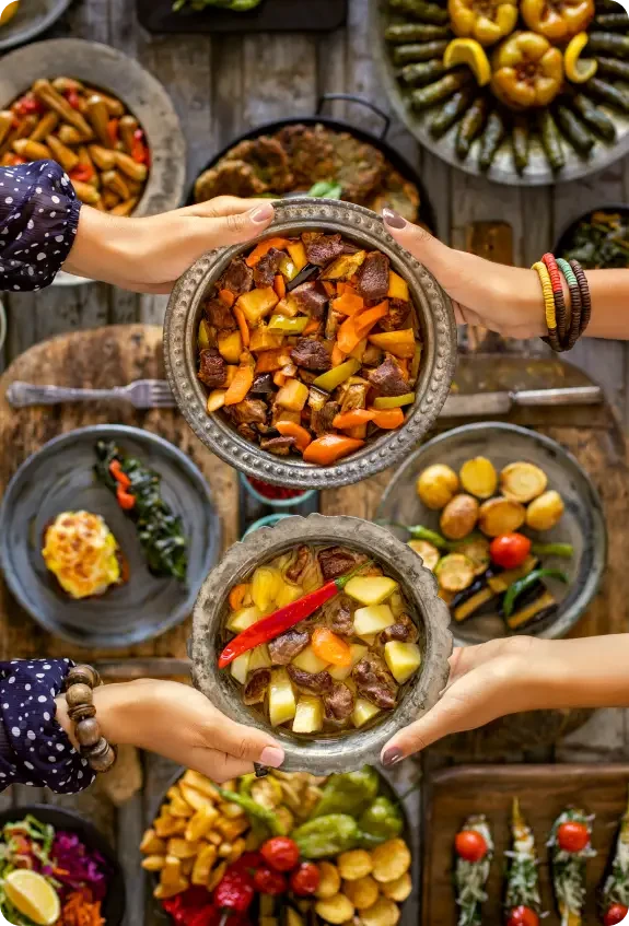 Hands sharing dishes of colourful cooked food across a table
