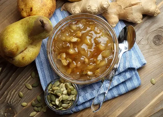 A jar of chunky pear preserve beside pears, ginger and spices