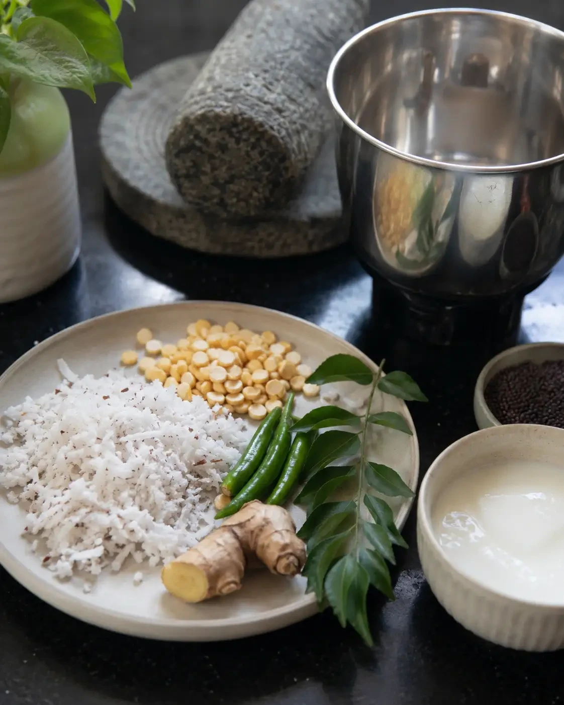 Grated coconut, chillies, herbs and spices beside a mortar and mixer jar